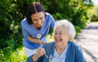 Female caregiver and senior woman in wheelchair holding dandelion