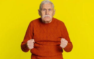 Senior man displaying frustration and aggression while looking at the camera against a yellow backdrop.