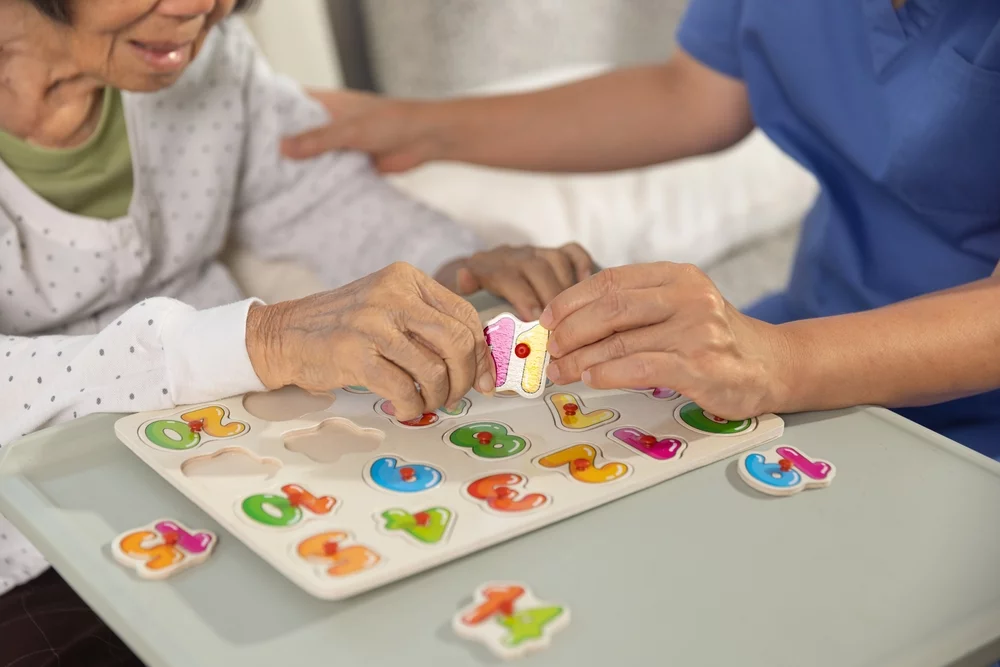 Nurse in memory care center helping a senior woman with number puzzle.