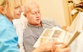 Caregiver and senior man reviewing photo album in a residential setting.
